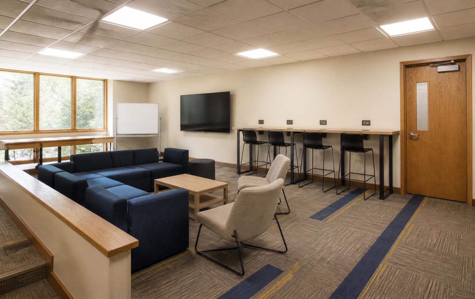 Perimeter touchdown counter with stools fed from existing outlets, modular navy sofa cluster, mobile whiteboard and a single wall display